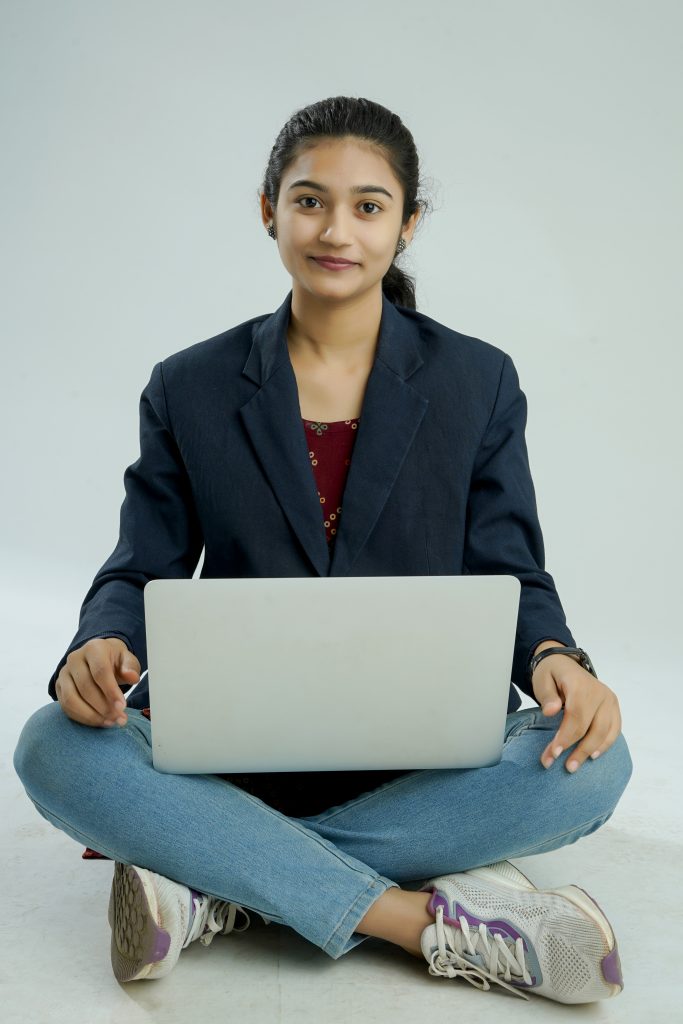 indian girl seated on a white background balances a laptop on her lap
